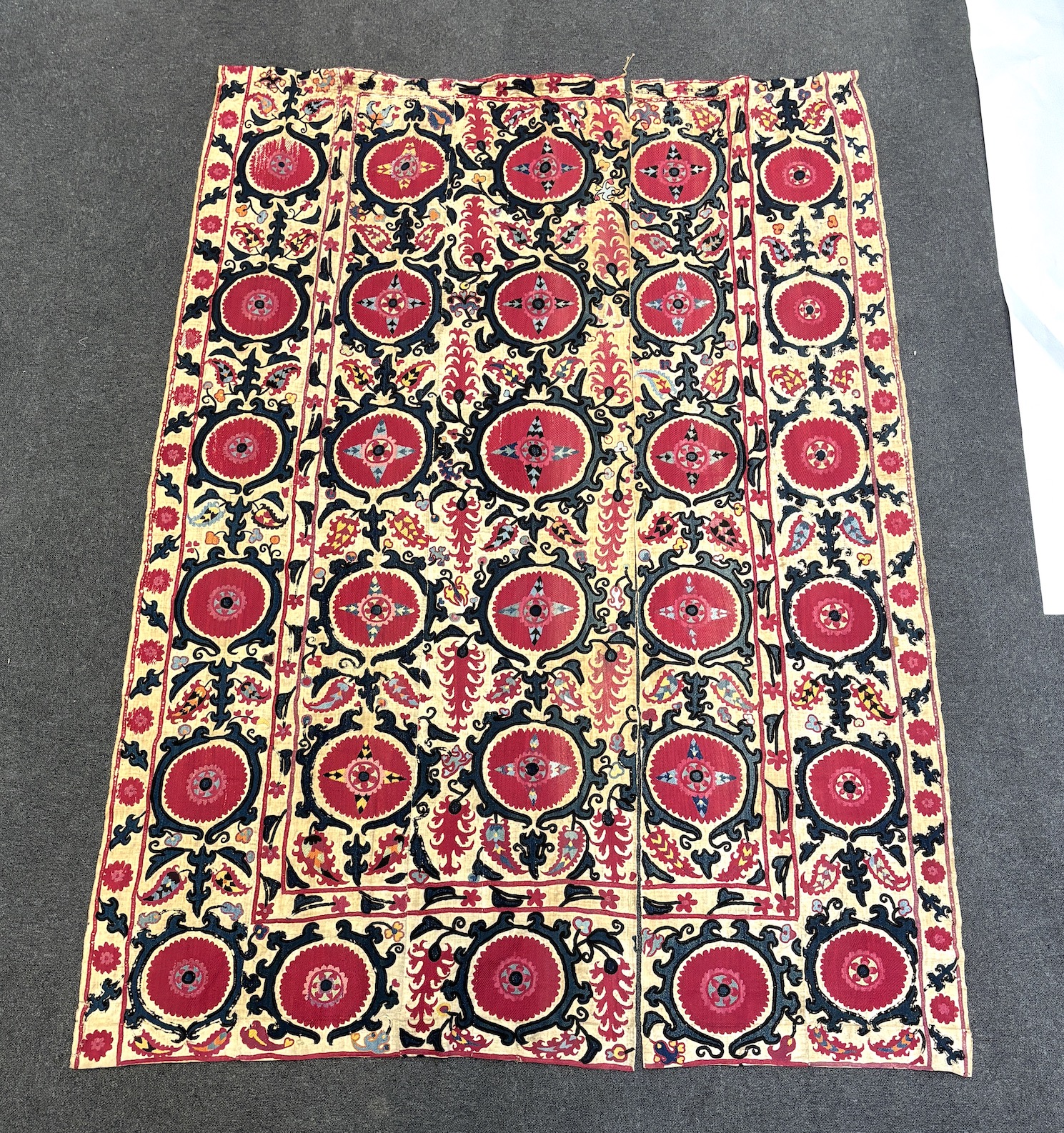 An 19th century Uzbek Suzani embroidered wall hanging, in two pieces, the main hanging sewn together as four panels, together with a fifth matching border, being detached, embroidered with large bold floral motifs, in ri